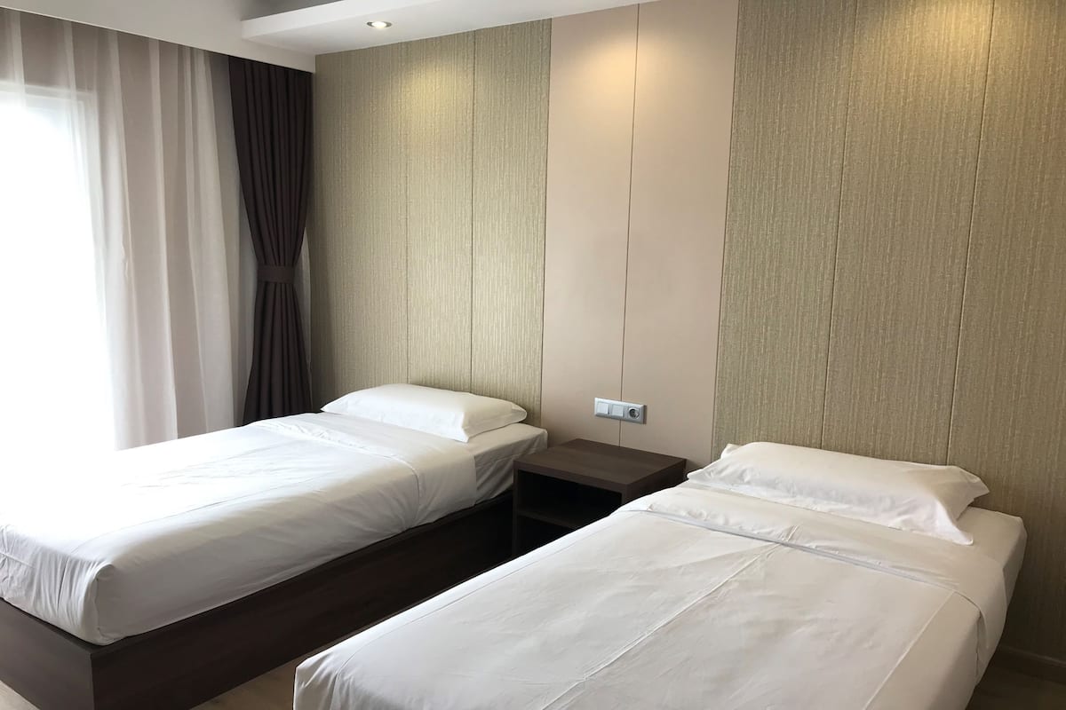 Une chambre d’hôtel avec deux lits simples, une table de chevet et un panneau de commande fixé au mur.