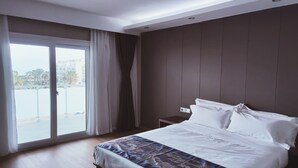 A modern hotel room with a large bed, a small bedside table, and a view through a sliding glass door to the outside. - Hotel Nueva Europa (Torredembarra)