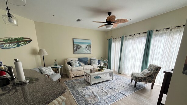 A living room with a sofa, coffee table, and a rug. There's a ceiling fan, a lamp, and a sign on the wall. - Ocean breeze treetops 2 bdrm walk to beach tennis dog friendly w/d permit#070894 (Hilton Head Island)