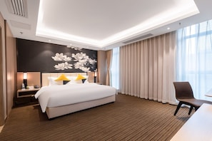 Une chambre d’hôtel avec un grand lit, un bureau avec une chaise, une lampe fixée au mur et une fenêtre avec des rideaux.