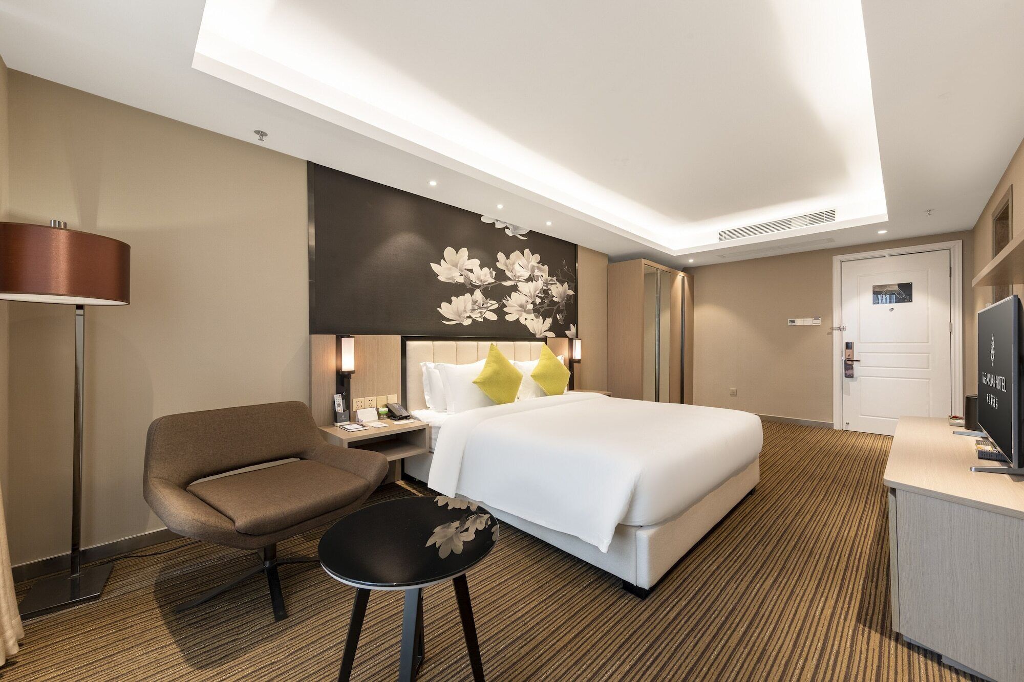 A hotel room with a bed, a desk, a chair, a small table, and a TV.