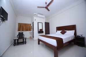 A hotel room with a bed, a desk, a chair, a TV, a ceiling fan, and an air conditioning unit.