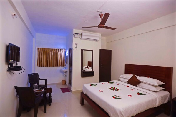 A hotel room with a bed, a desk with a chair, a television, an air conditioning unit, and a ceiling fan. - Rani Residency (Vanur)