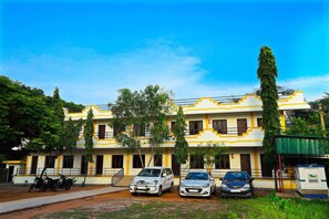A multi-story building with a yellow and white facade, parked cars, and trees in front.