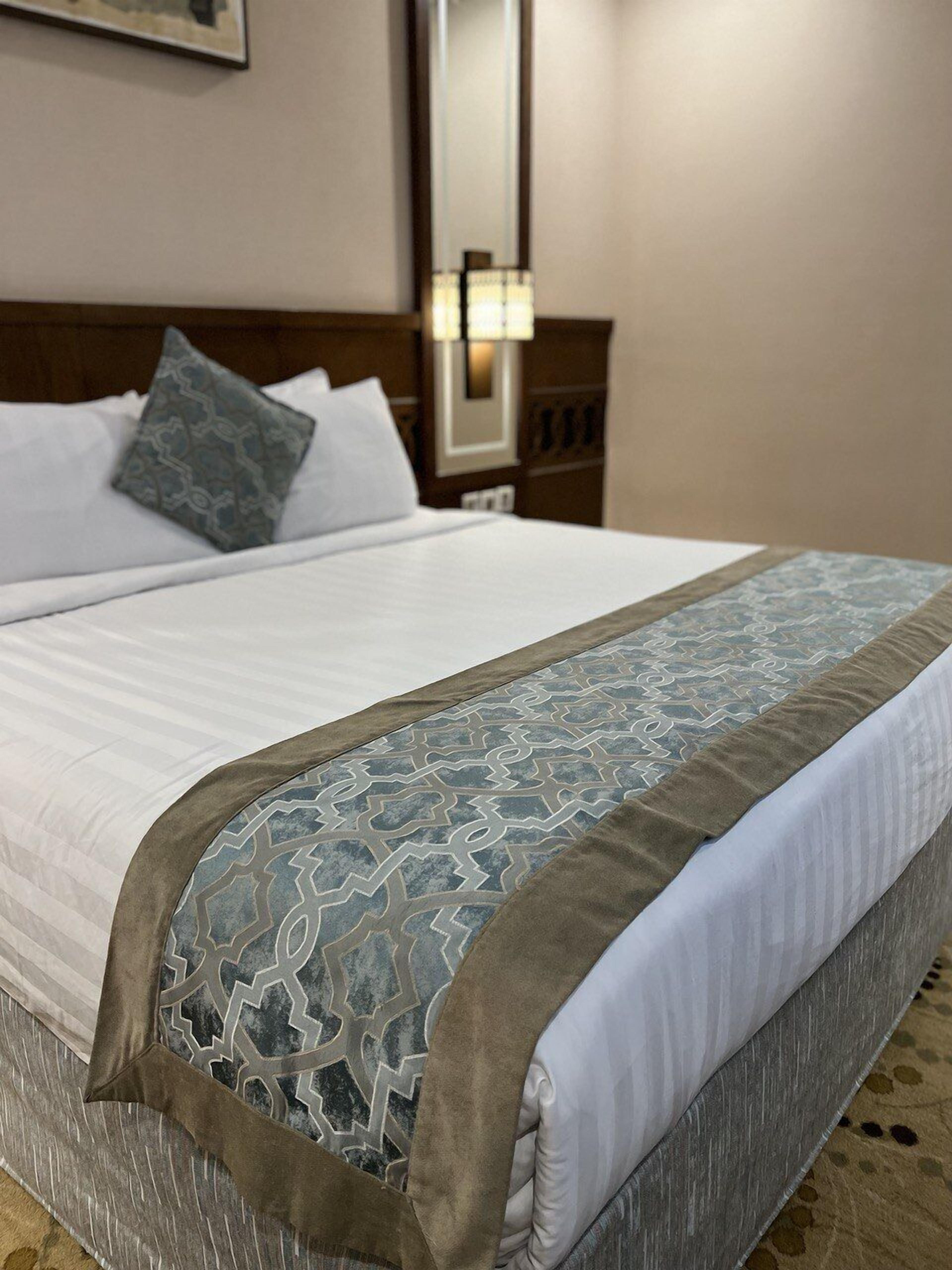 A neatly made bed with a patterned bedspread and pillows, a wooden headboard, and a nightstand with a lamp.