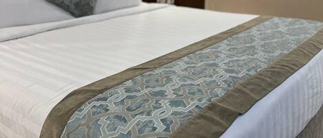 A neatly made bed with a patterned bedspread and pillows, a wooden headboard, and a nightstand with a lamp.