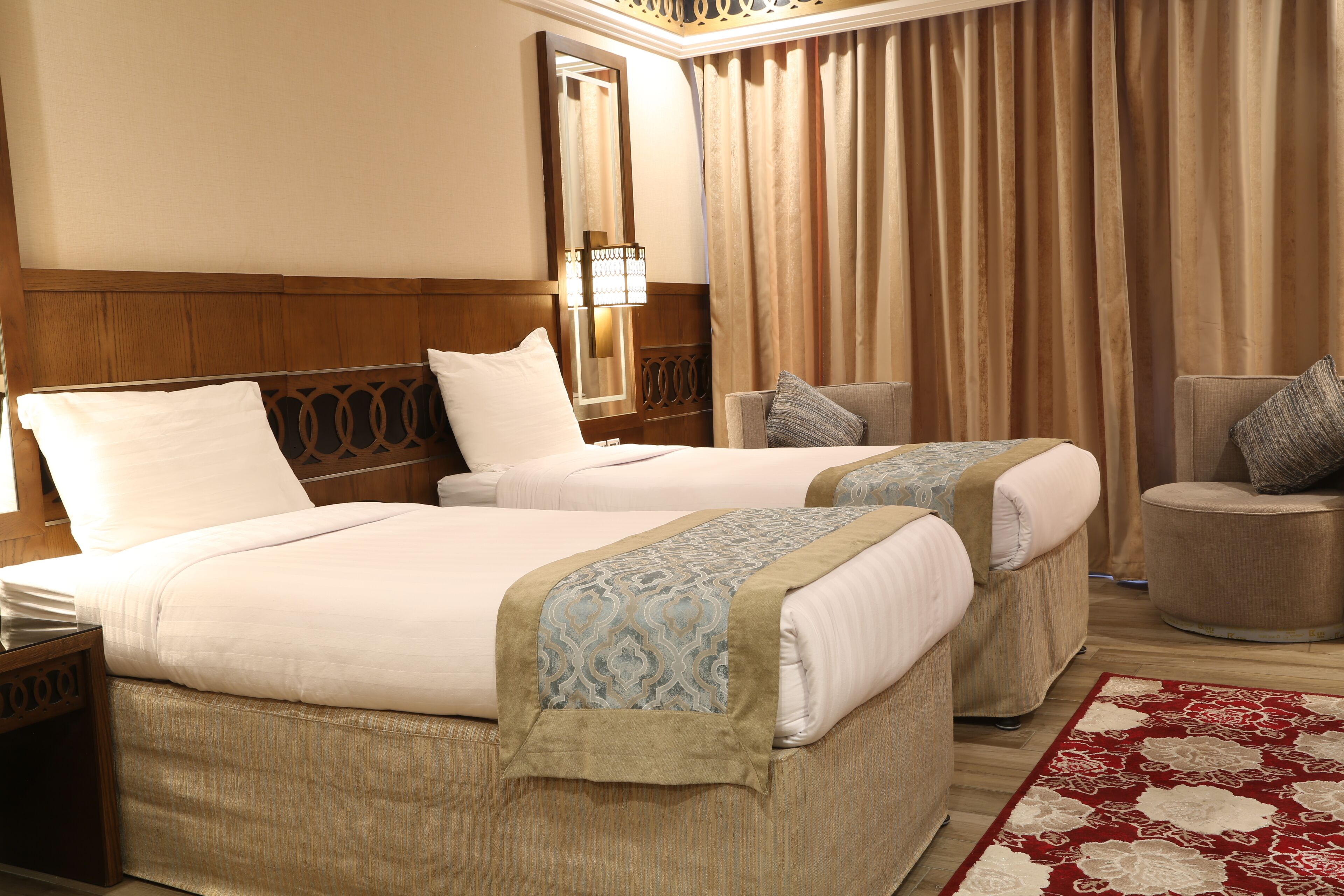 A hotel room with two beds, a sitting area, a mirror, and a window with curtains.