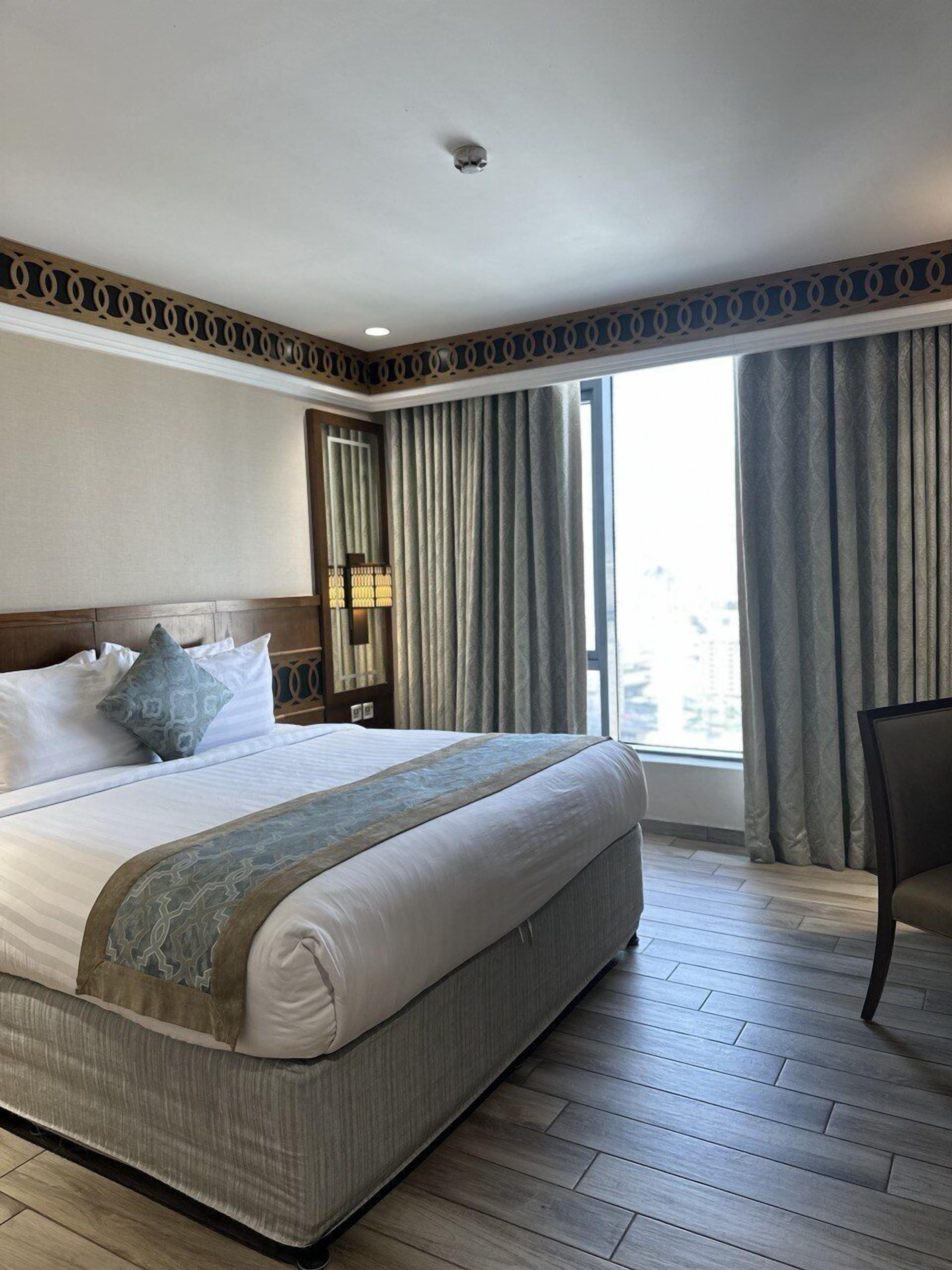 Camera d'albergo con un letto grande, un comodino, una lampada e vista sulla città dalla finestra.