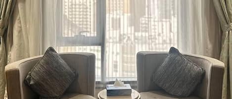 A room with two armchairs facing a large window, a small round table, and a decorative metal lamp.