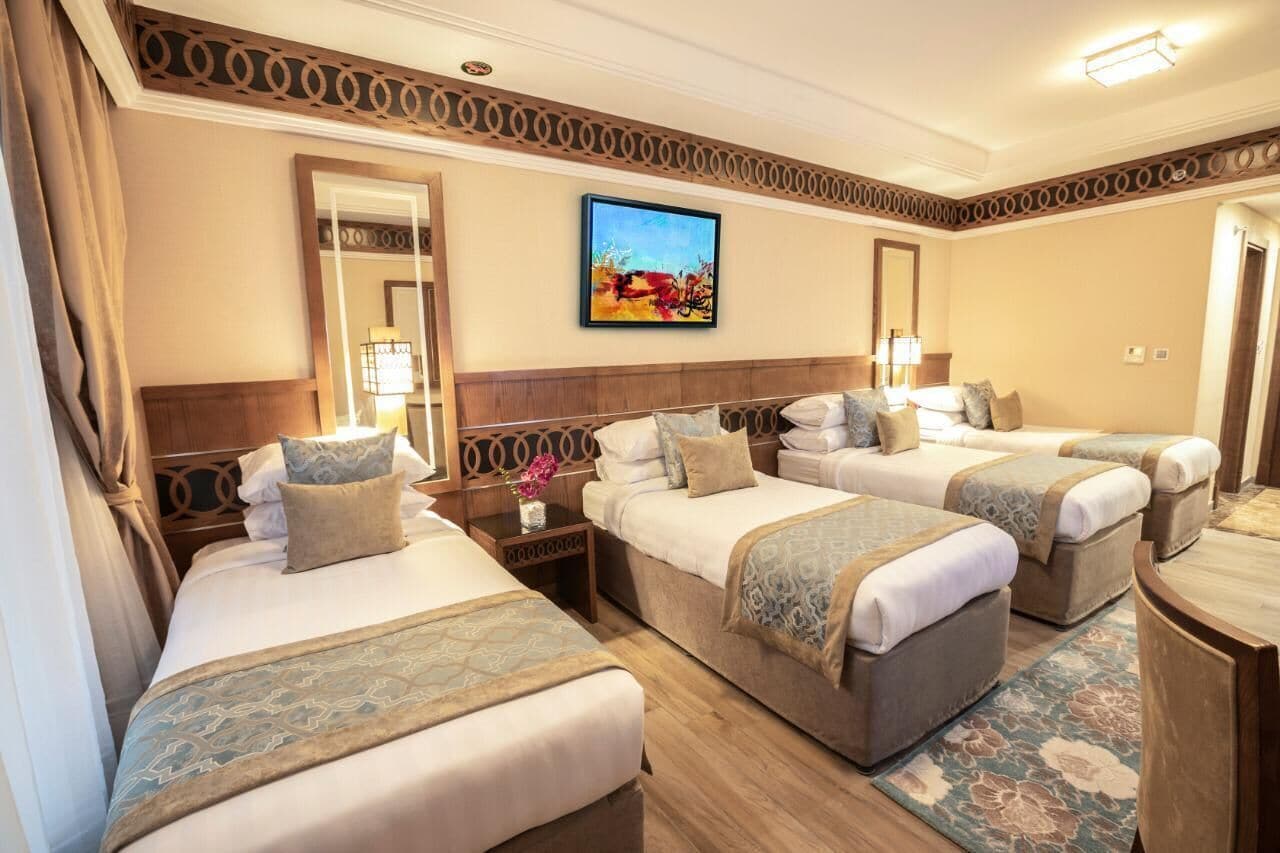 Une chambre d’hôtel avec trois lits, un grand miroir, un tableau au mur et une tête de lit en bois.