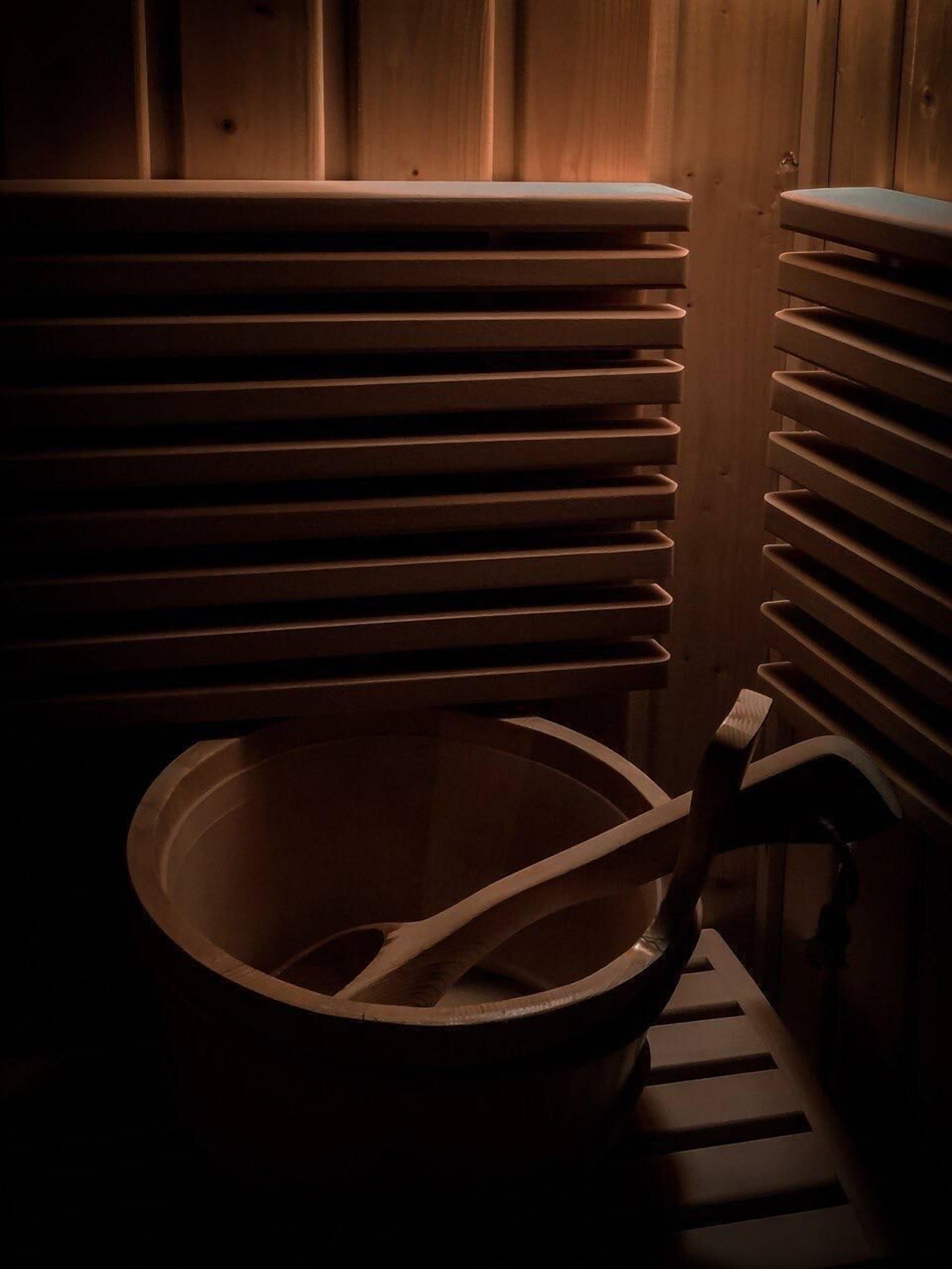 A sauna with multiple benches and a large wooden bowl.