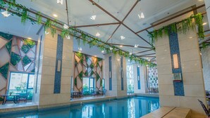 En indendørs swimmingpool med fliserede vægge, hængende planter og geometriske vægmotiver.