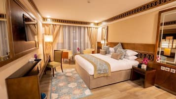 A hotel room with a large bed, a desk, a chair, a TV, and a mirror.