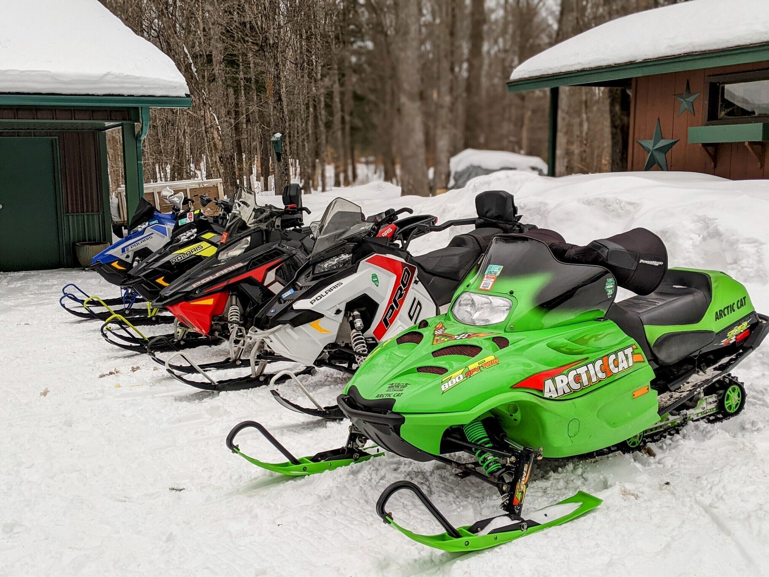 A row of snowmobiles parked in a snowy outdoor area with a building in the background.