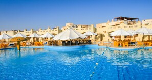 A swimming pool with sun umbrellas and lounge chairs, surrounded by buildings with a traditional architectural style.