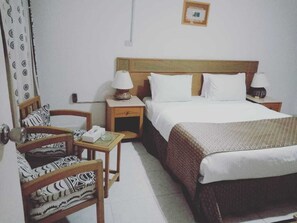 A hotel room with a bed, two bedside tables with lamps, a chair, and a small table with a tissue box.
