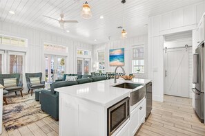A spacious kitchen with a large island, white cabinetry, and a dining area with green upholstered chairs.