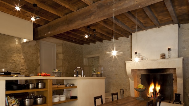 A rustic kitchen with exposed wooden beams, a fireplace, and a dining table with chairs.