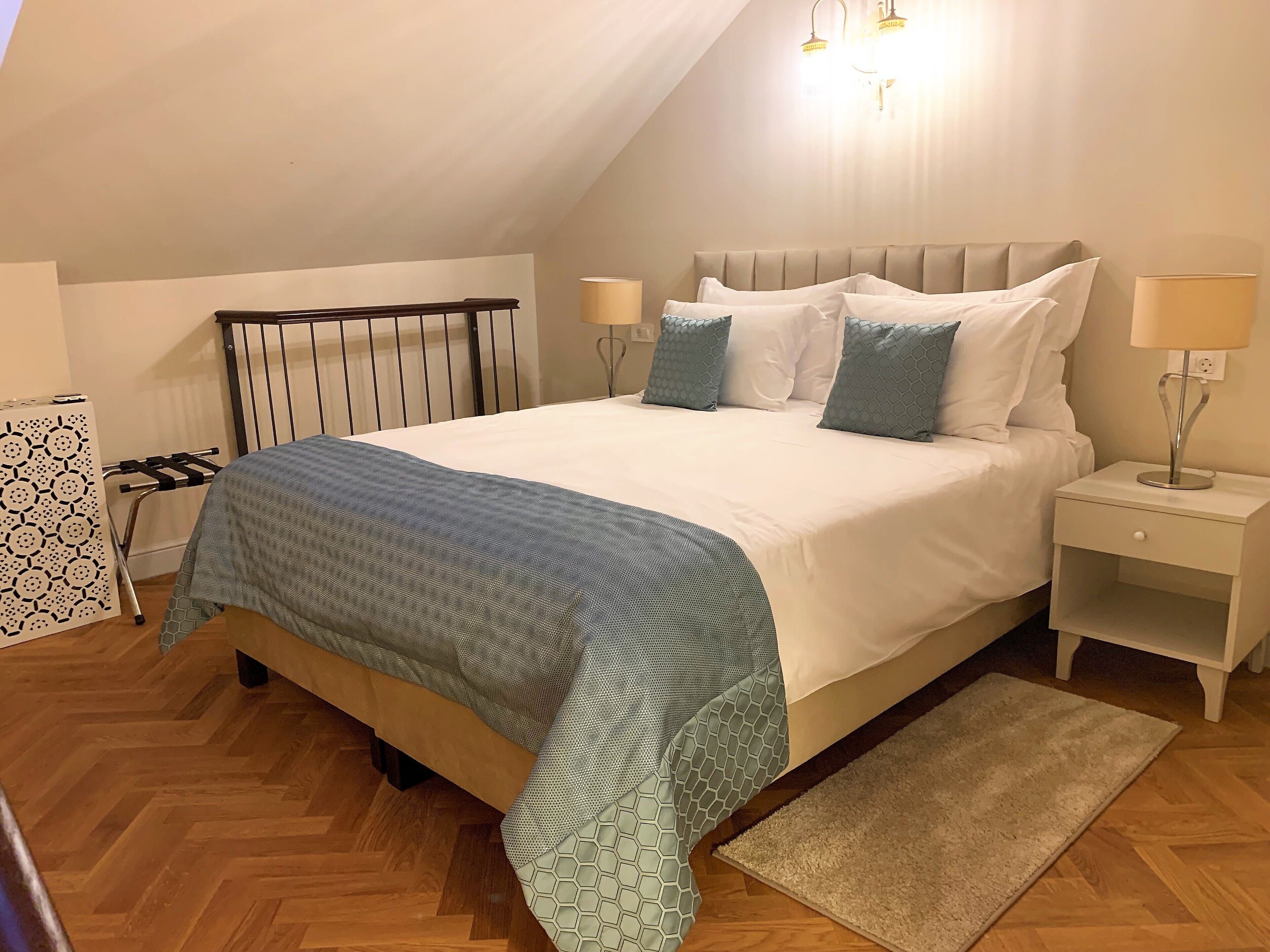Un dormitorio con cama, mesitas de noche, lámpara, panel decorativo en la pared y suelo con estampado de espiga.