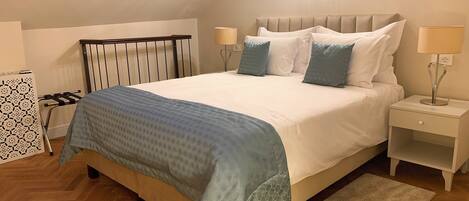 Un dormitorio con cama, mesitas de noche, lámpara, panel decorativo en la pared y suelo con estampado de espiga.
