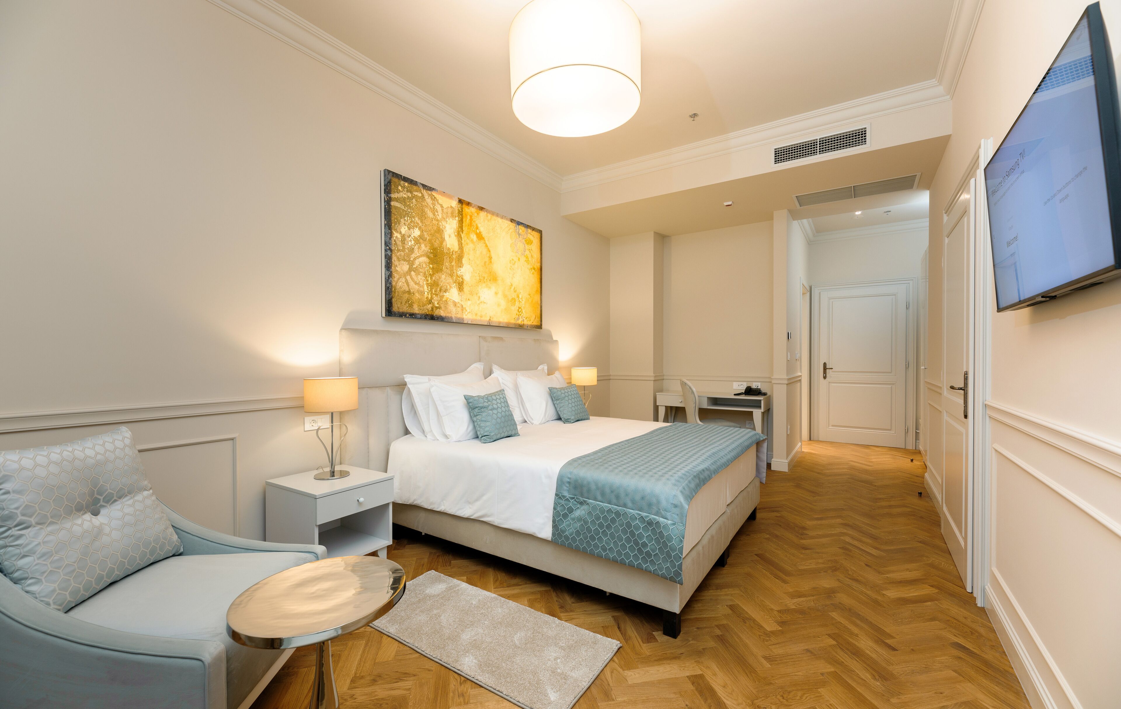 A hotel room with a bed, a chair, a desk, and a TV on the wall.