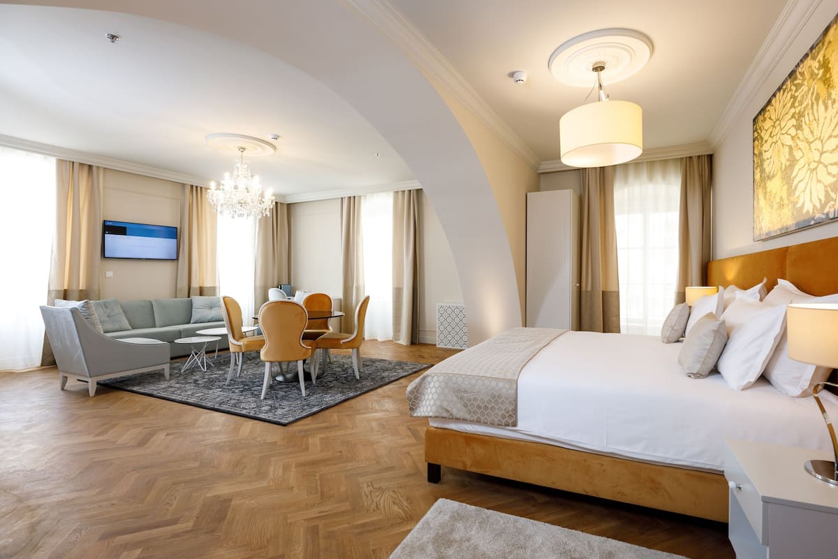 A hotel room with a bed, a sofa, a dining table, and a chandelier.
