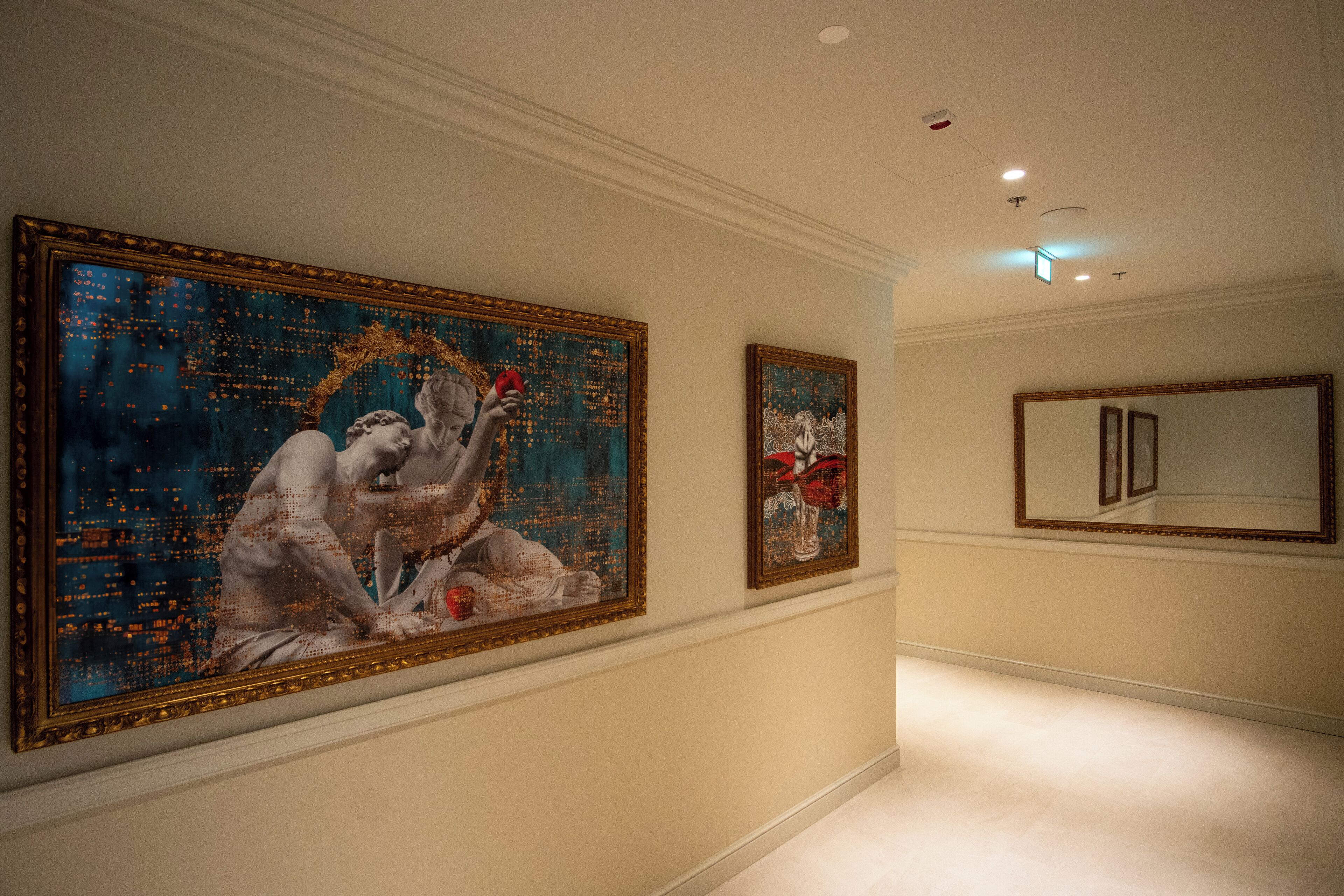 A hallway with two large framed paintings on the walls, a mirror, and a light ceiling.