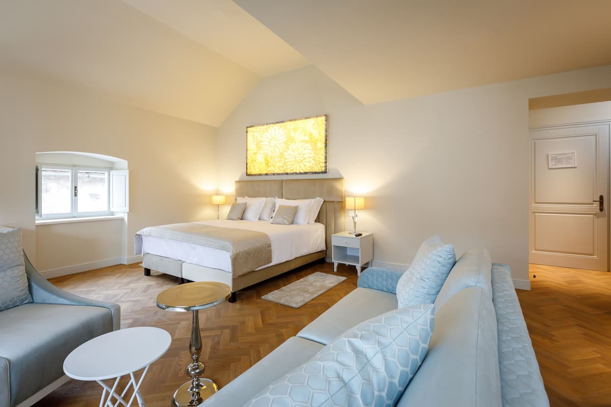 A modern bedroom with a large bed, bedside tables, a sofa, and a small round table.