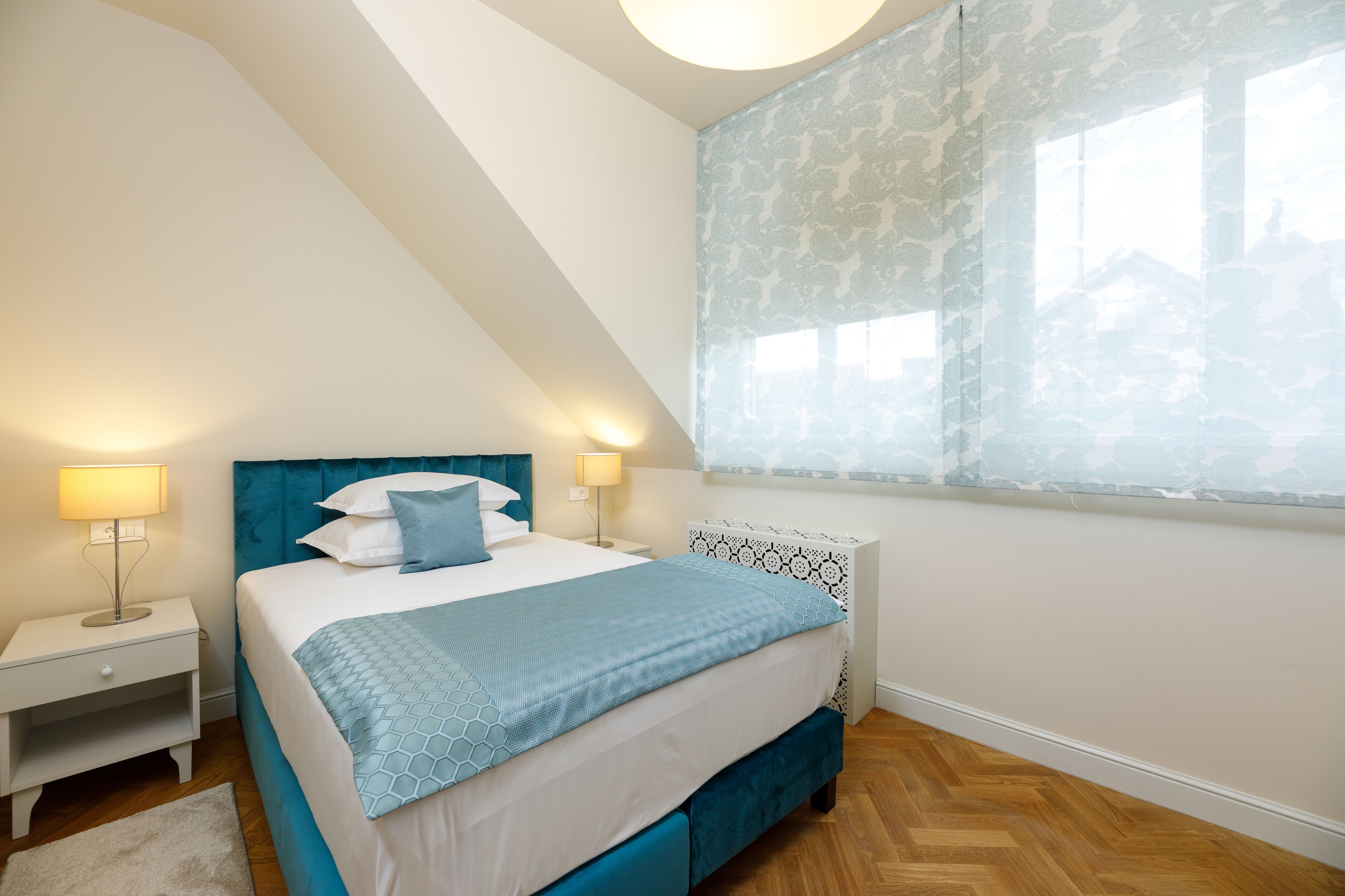 Een slaapkamer met een bed, nachtkastjes en een raam met patroon gordijnen.