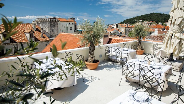 Una terraza en la azotea con asientos al aire libre, olivos en macetas y vistas de la ciudad.