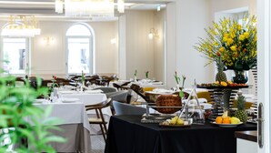 Un restaurante con mesas dispuestas para comer, un bufé de frutas y verduras, y un jarrón decorativo con flores amarillas.