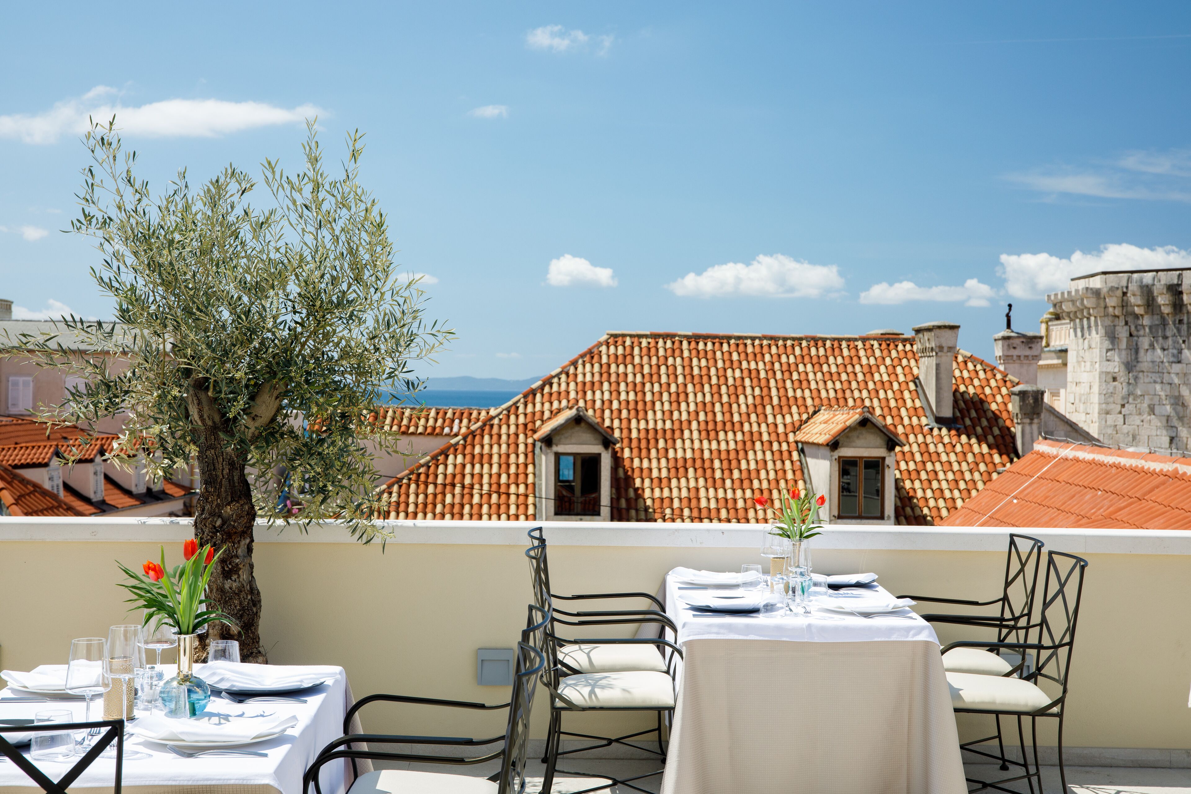 A rooftop terrace with a table set for dining, overlooking a cityscape with terracotta-roofed buildings.