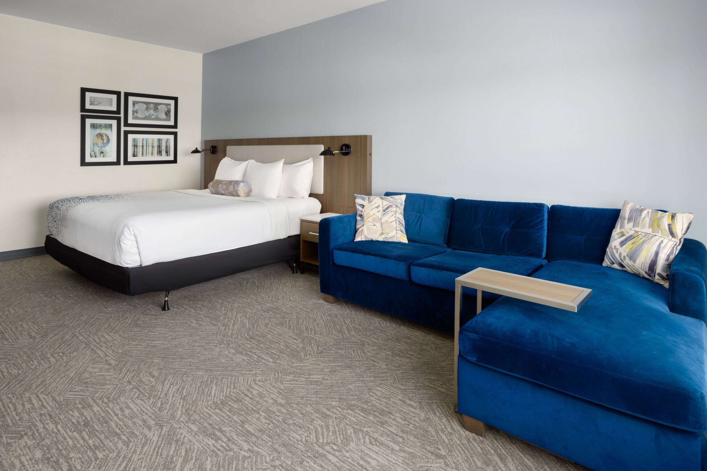 Ein modernes Hotelzimmer mit einem Bett, einem blauen Sofa, einem kleinen Tisch und gerahmten Bildern an der Wand.