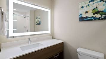 A bathroom with a large mirror, a sink, a toilet, and a wall-mounted painting.