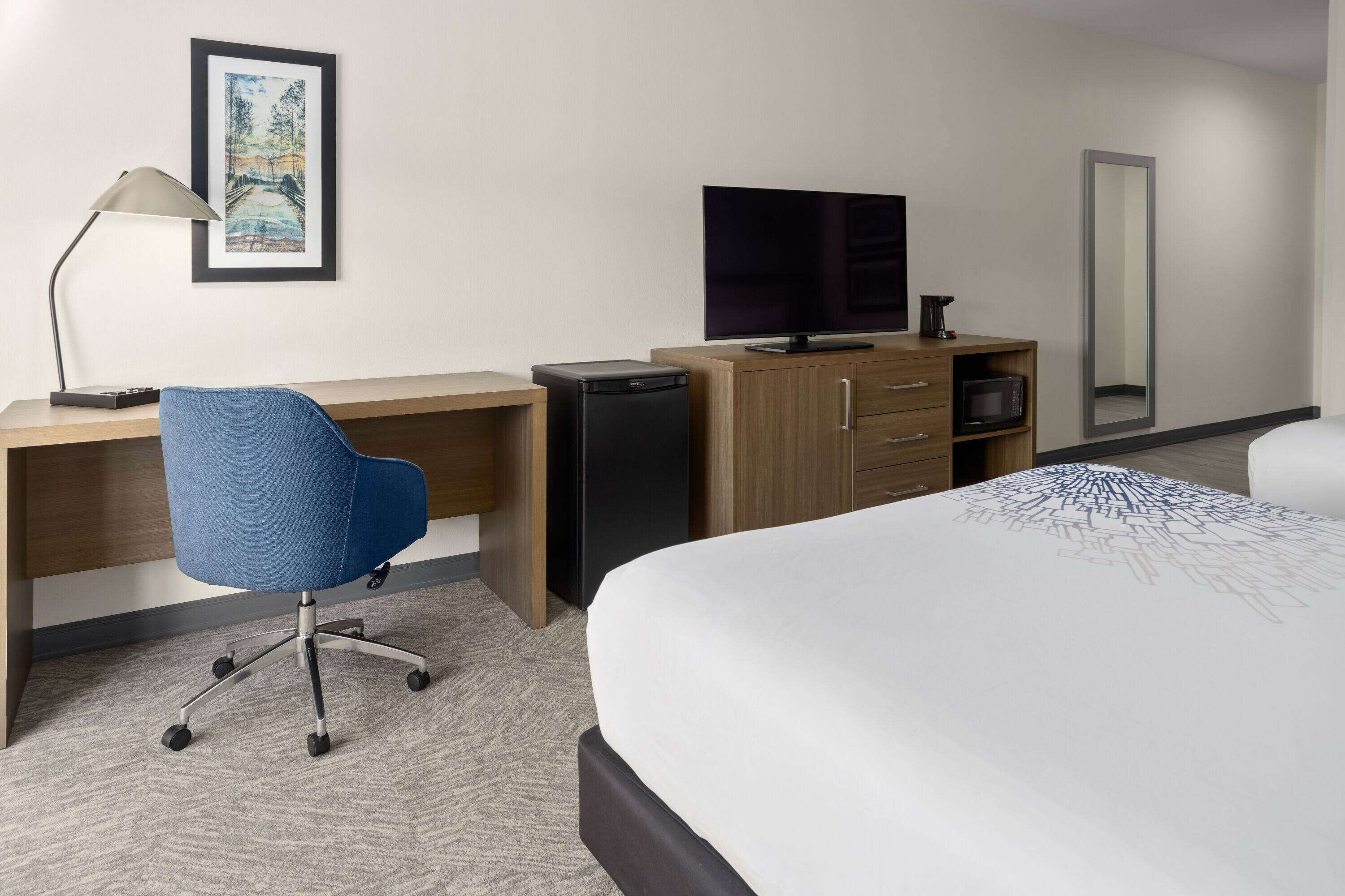 Een hotelkamer met een bed, bureau, stoel, televisie en een kleine koelkast.