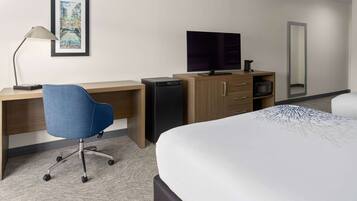 A hotel room with a bed, desk, chair, television, and a small refrigerator.