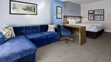 Ein Zimmer mit einem blauen, modularen Sofa, einem Holztisch, einem Einzelbett und gerahmten Kunstwerken an den Wänden.