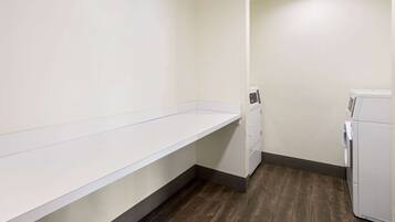 A laundry room with a white washing machine, a drying machine, and a long white bench.