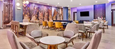 Ein moderner Lounge-Bereich mit bequemen Sitzgelegenheiten, einem runden Tisch in der Mitte und einer Wandmalerei.
