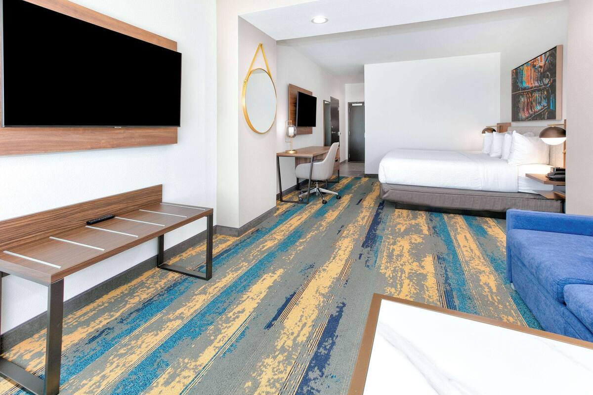 A hotel room with a large bed, a desk with a chair, a television mounted on the wall, and a painting on the wall.