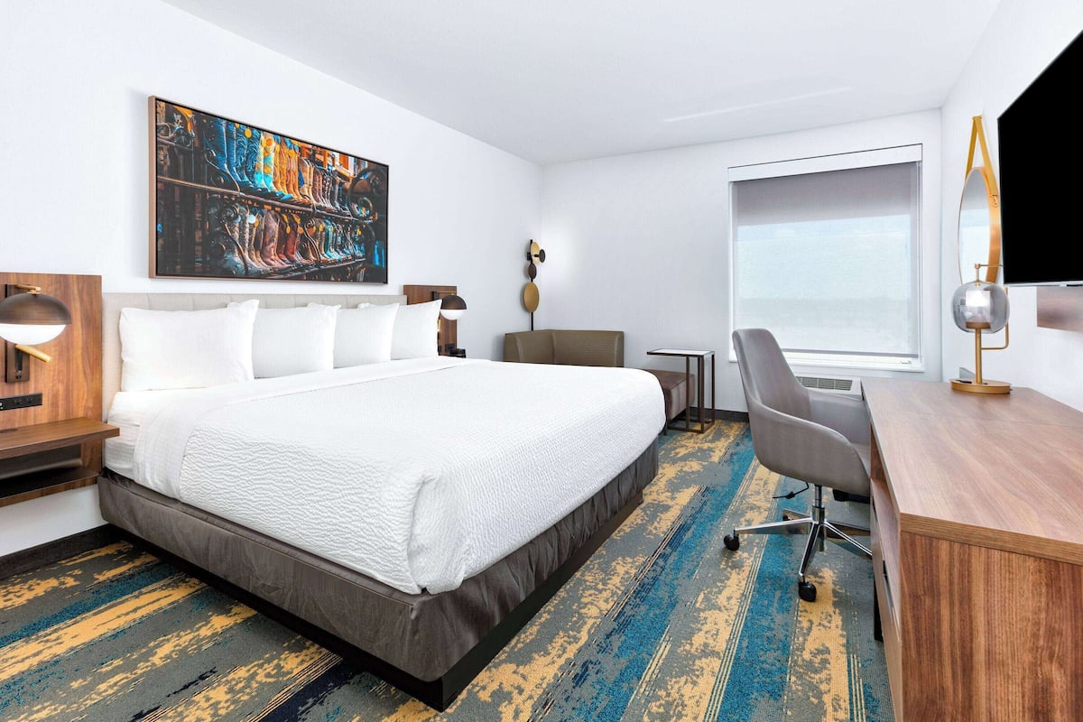 A hotel room with a large bed, a desk, a chair, a TV, and a painting on the wall.
