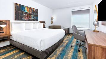 A hotel room with a large bed, a desk, a chair, a TV, and a painting on the wall.