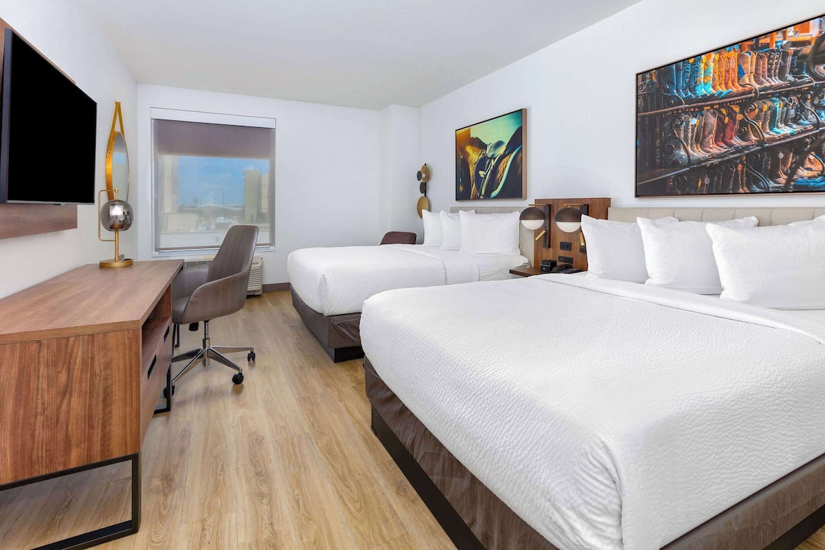 A hotel room with a bed, a desk, a chair, a TV, and artwork on the walls.