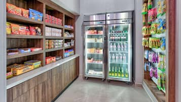 Una sección de aperitivos y bebidas con estantes llenos de diferentes productos y dos vitrinas refrigeradas.