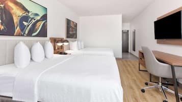 A hotel room with two beds, a desk, a chair, a flat-screen TV, and artwork on the walls.