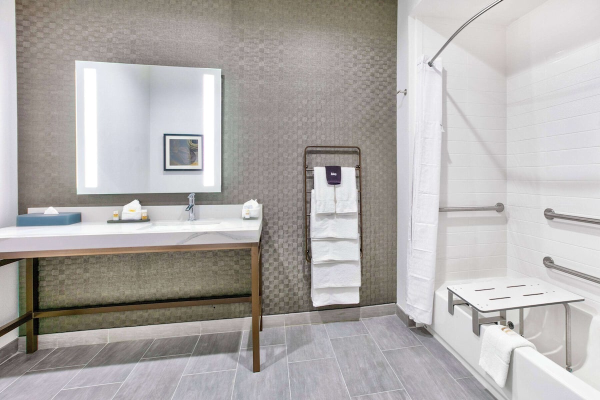 A modern bathroom with a vanity, a large mirror, a shower with a grab bar, and a towel rack.