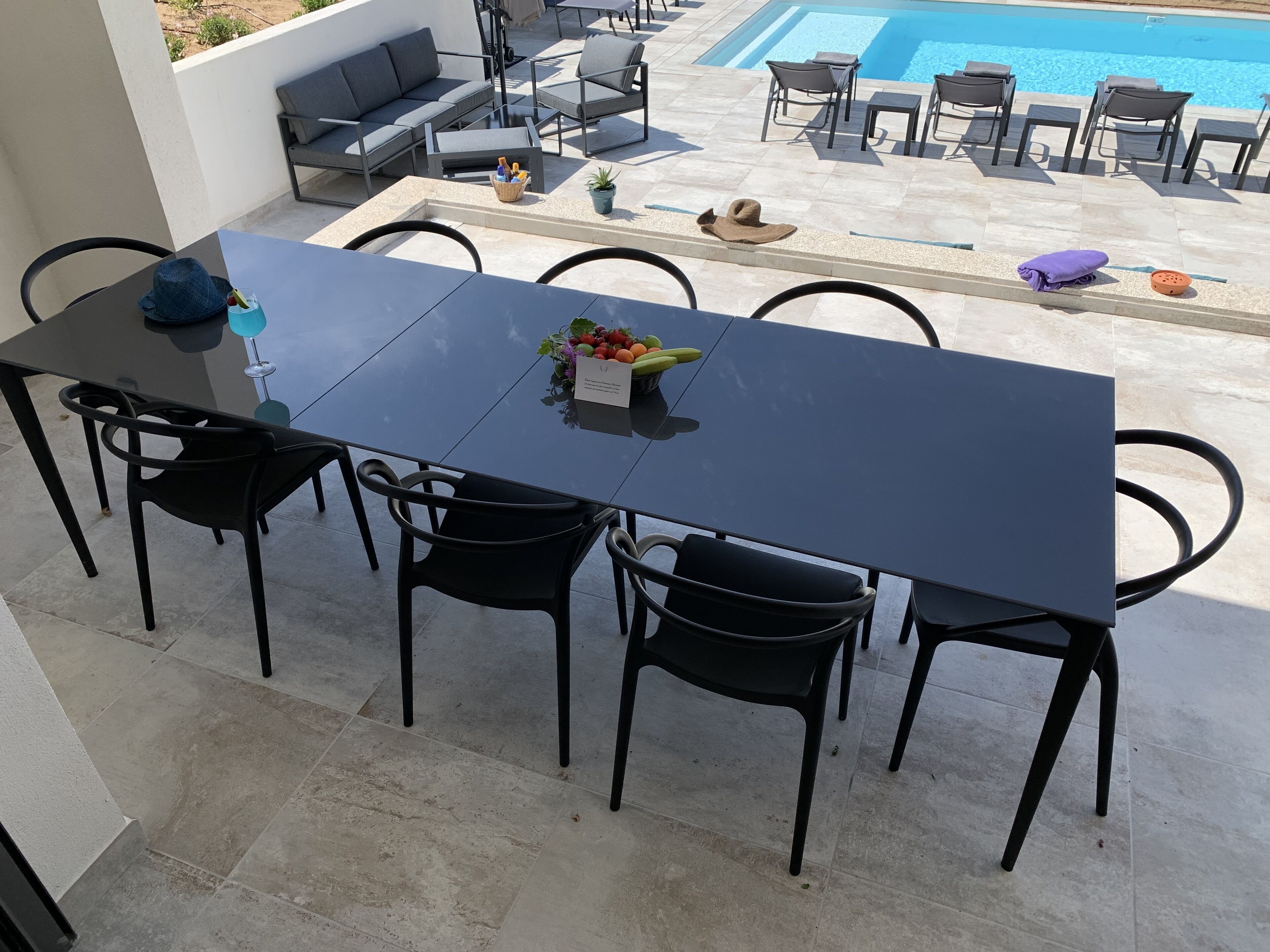 Un comedor con una mesa y sillas negras, una planta pequeña en maceta y una cesta de fruta.