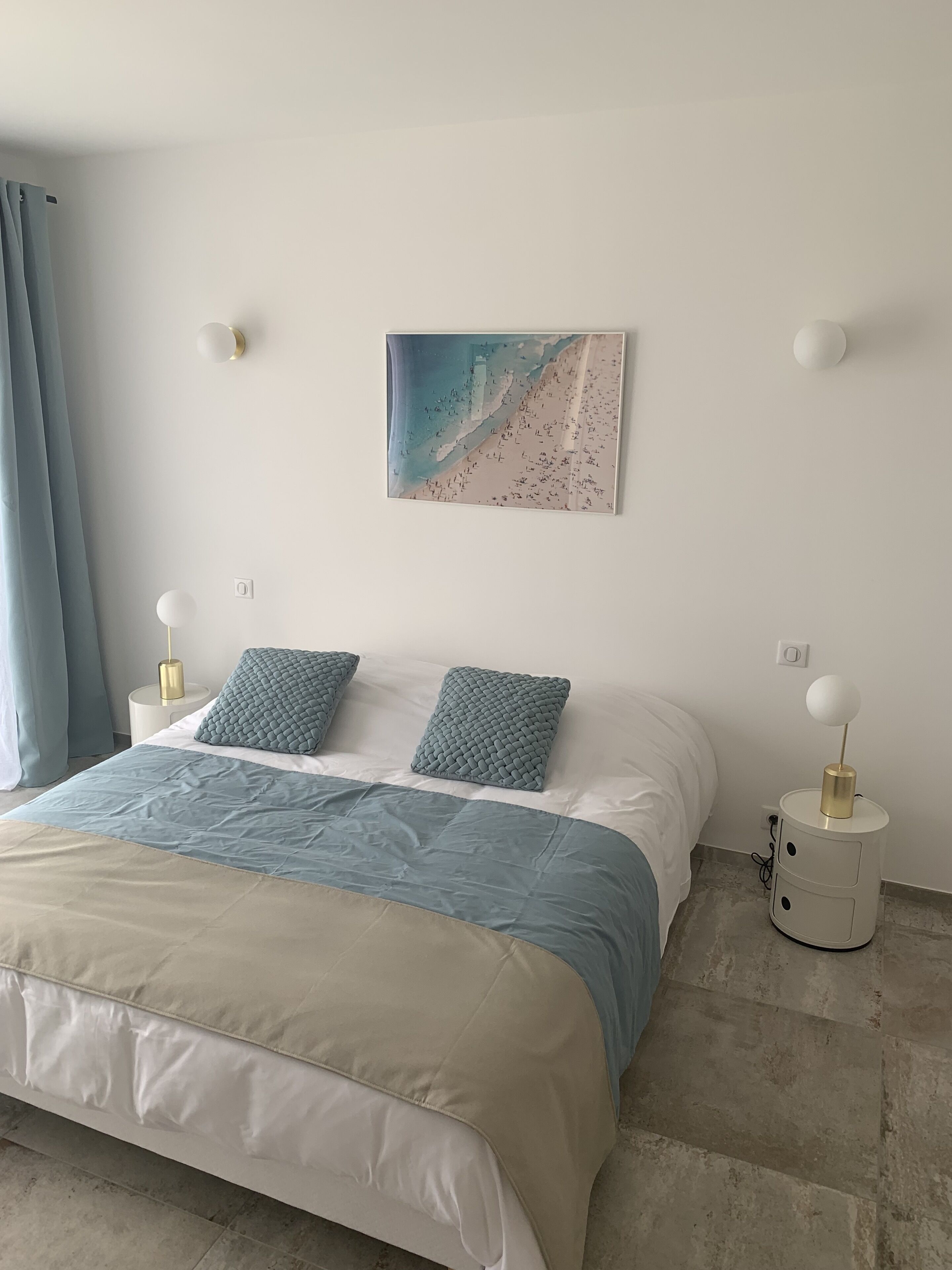 Ett sovrum med en säng, två sängbord, en vägglampa och ett konstverk med strandtema.