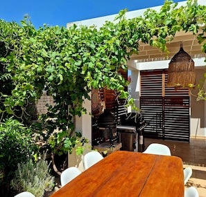 Un patio con mesa y sillas de madera, una parrilla y una pérgola cubierta de parras.