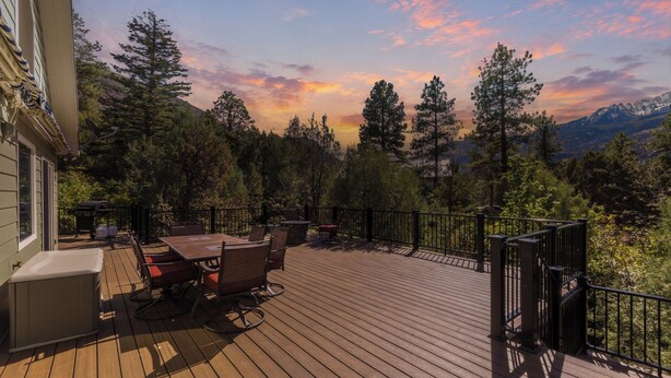 A wooden deck with outdoor furniture, surrounded by trees and mountains in the background. - Secluded Creekside Home | Incredible Views | A/C | Private Deck | STR2025-036 (Ridgway)